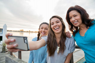 Three friends laying in the snow taking a selfie with a cell phone